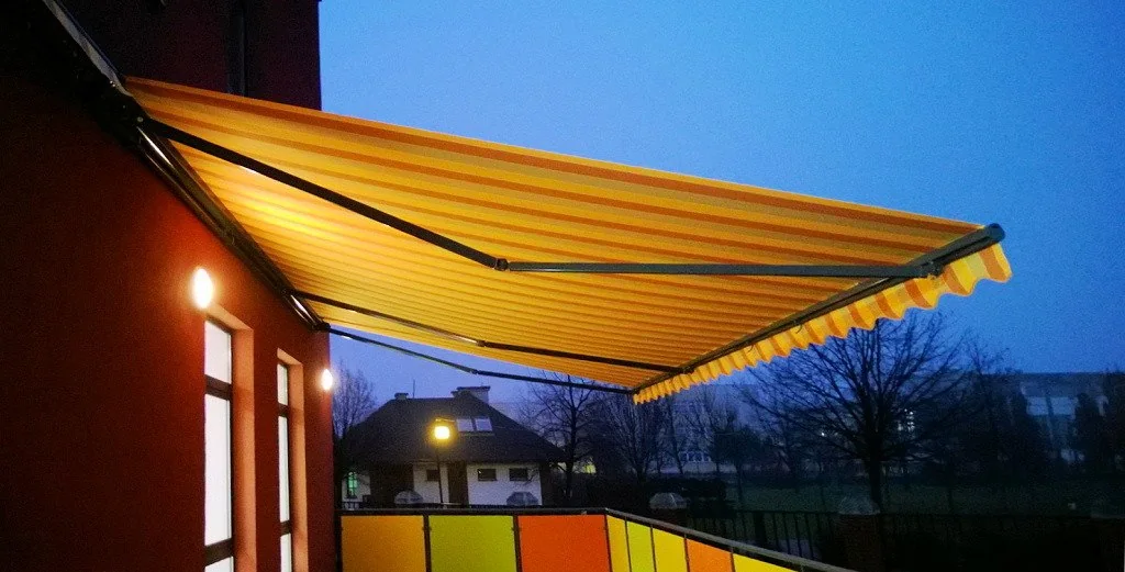 Stripete terrassemarkise over en opplyst uteplass om kvelden